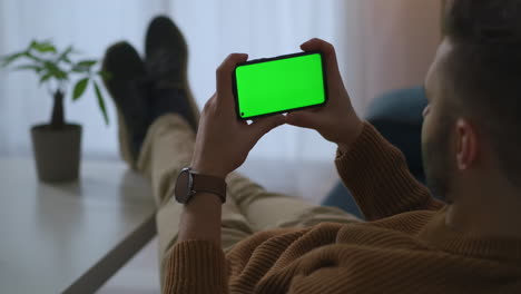 adult-man-is-looking-on-display-of-modern-smartphone-with-green-screen-technology-relaxing-and-viewing-video-at-break-time-in-office-or-home